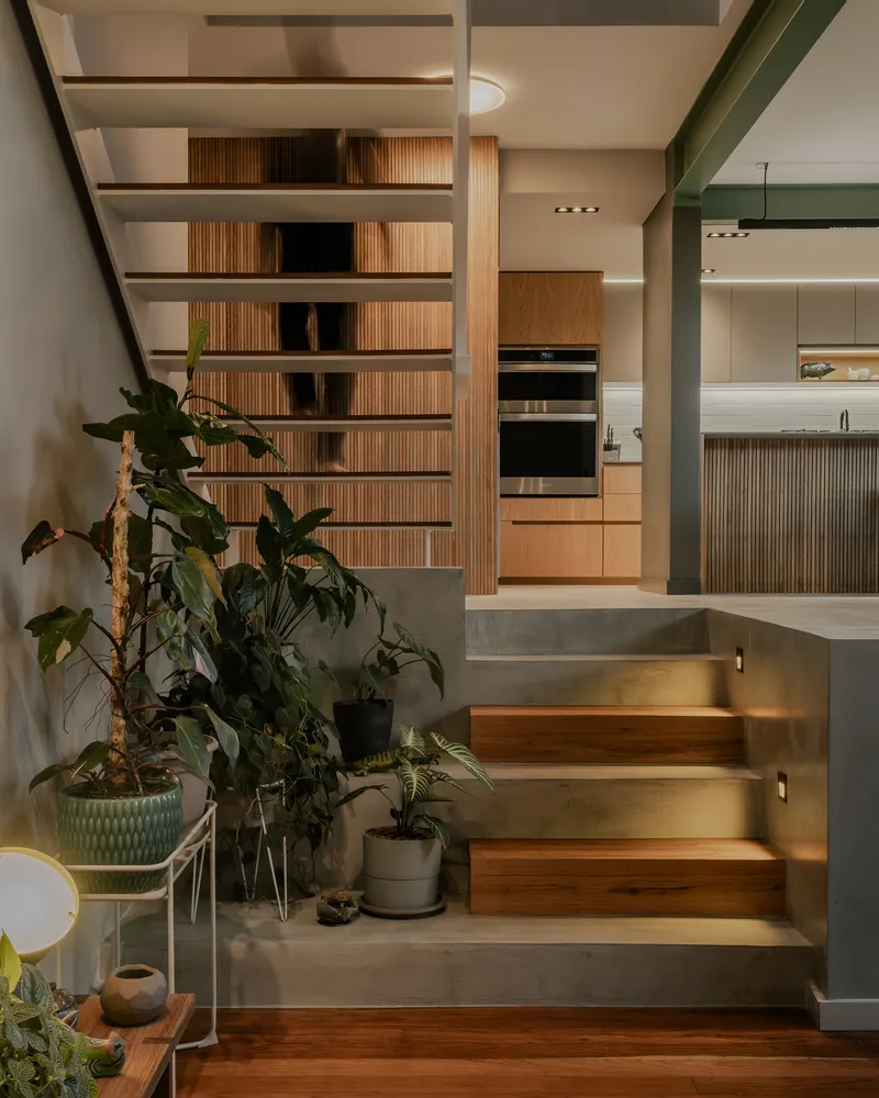 Interior staircase with timber treads and open slat shelving flanked by potted plants
