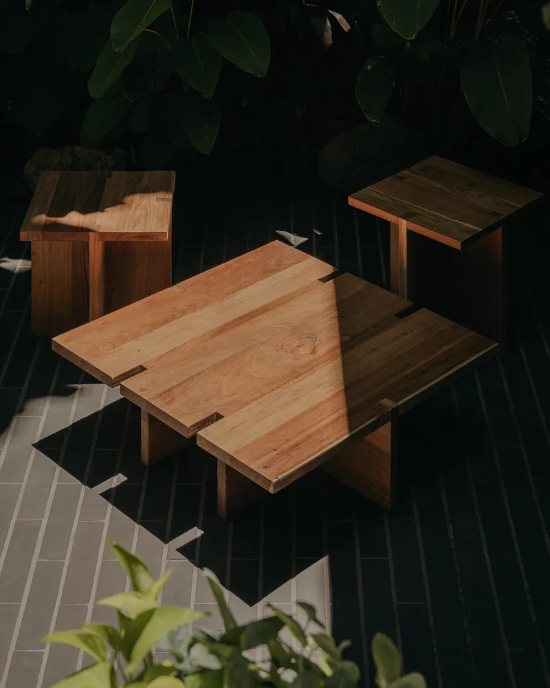 Overhead view of timber side tables on a dark tile terrace with tropical foliage