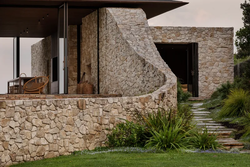 Curved stone retaining wall and exterior staircase beside a paved garden path with ornamental grasses