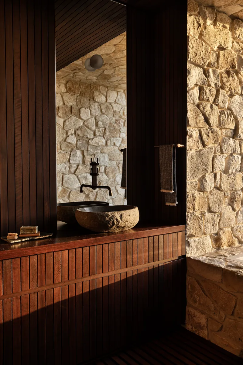 Bathroom vanity with timber slat cabinetry and stone vessel sink against coursed stone walls