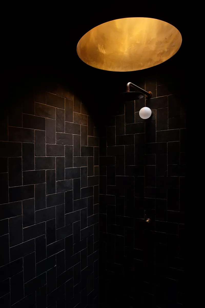 Shower enclosure with black staggered tile walls illuminated by backlit onyx skylight above