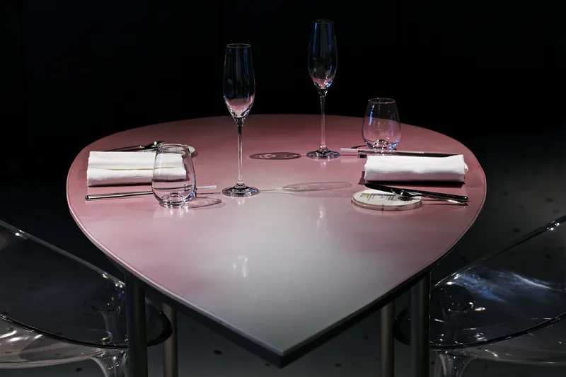 Heart-shaped pink table with place settings and glassware flanked by transparent acrylic chairs