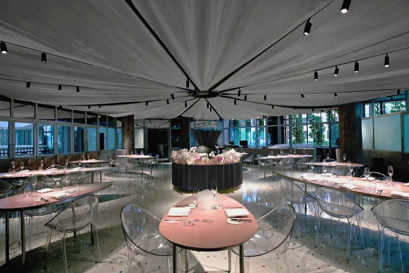 Restaurant dining room with radial fabric ceiling canopy and pink circular tables beneath track lighting