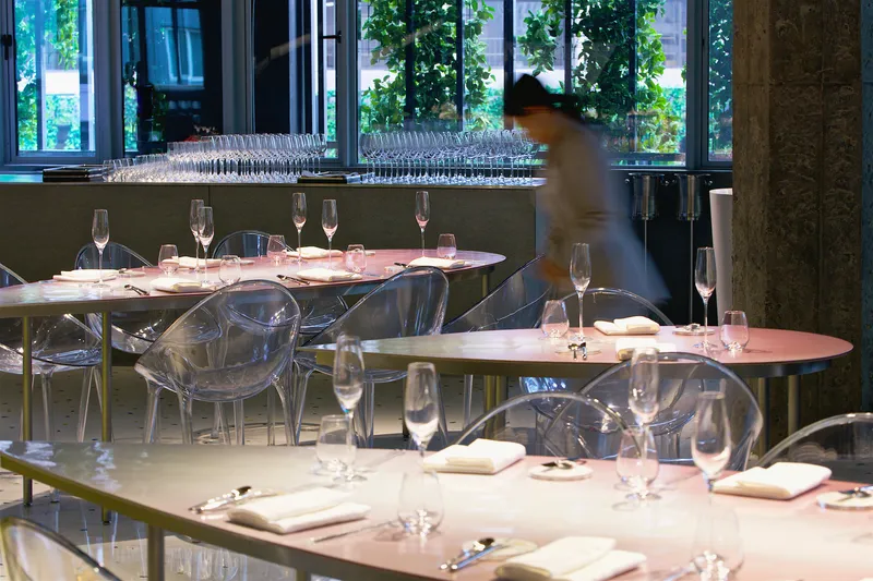 Pink table setting with transparent acrylic chairs and a blurred figure moving through the dining space