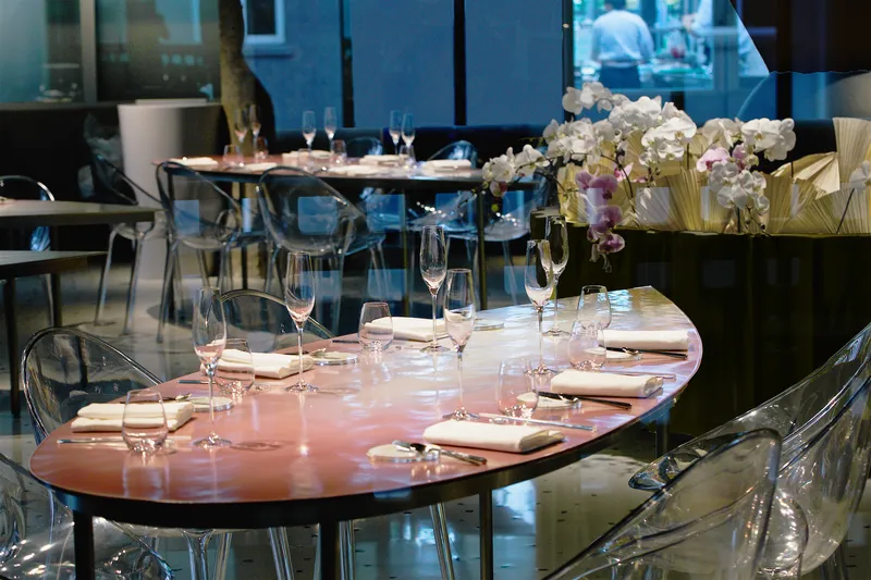 Close-up of a glossy pink table with orchid arrangement and place settings reflecting overhead light