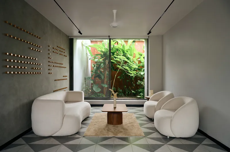 Sitting area with curved sofas and geometric floor tiles facing a window overlooking banana plants