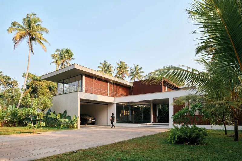 Street view of the two-level residence with red paneled upper facade and open carport beneath palm trees