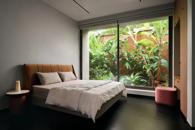 Bedroom with full-height glass doors opening to a planted garden bed with banana leaves