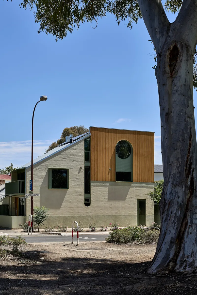 View from park showing timber upper storey and circular window framed by eucalyptus tree trunk