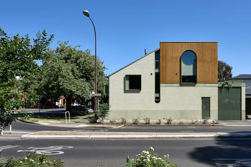 Street view of the two-storey facade with vertical timber cladding and circular window under clear blue sky