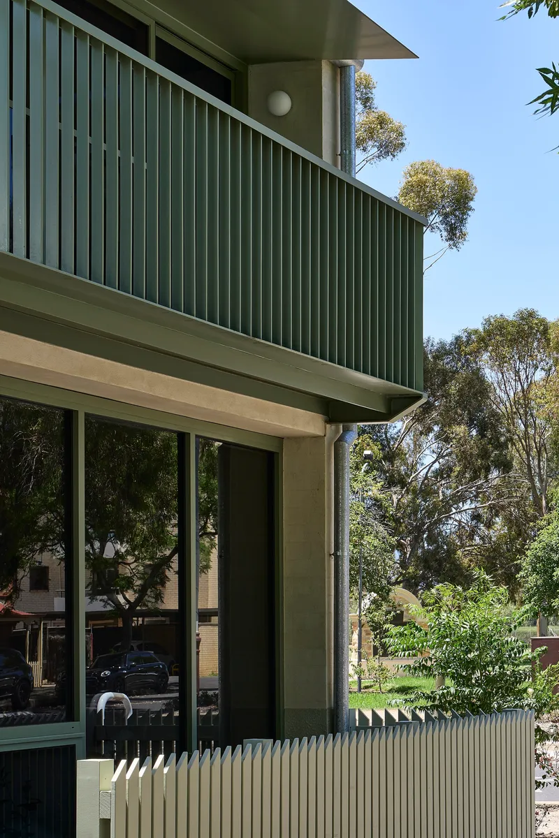 Cantilevered balcony with vertical green metal slat screen above full-height glazed doors