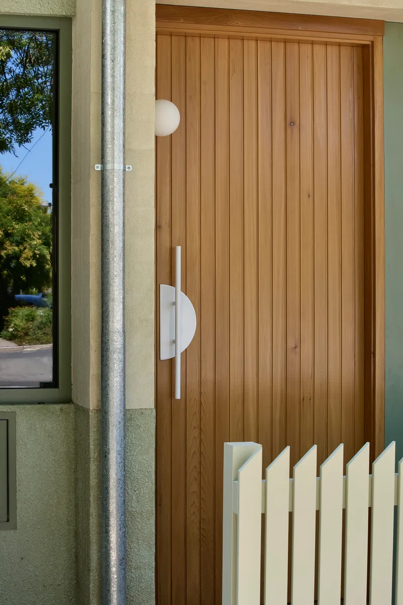 Vertical timber-clad entry door with white semicircular handle and adjacent concrete downpipe