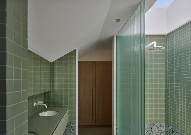 Bathroom interior with green square tile walls, fluted glass shower screen and terrazzo flooring