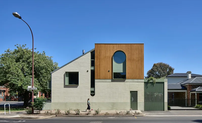Street facade with vertical timber cladding, round window, and pale render base with pedestrian passing