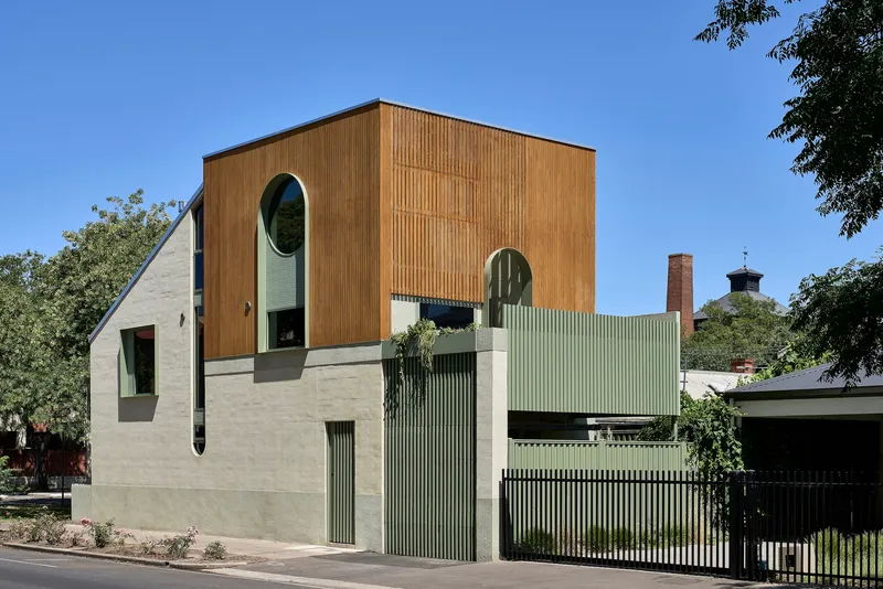 Corner view showing timber box volume above rendered podium with corrugated metal fence and gate