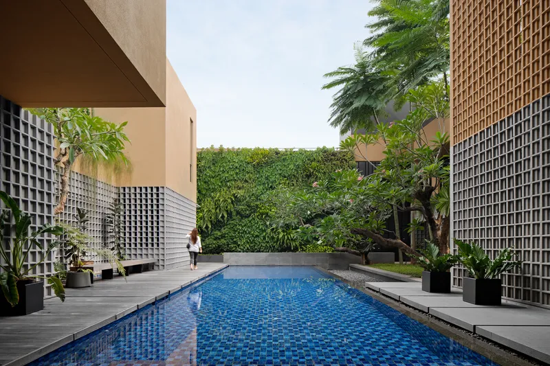 Blue-tiled lap pool flanked by lattice screen walls and a vertical garden beneath overcast skies