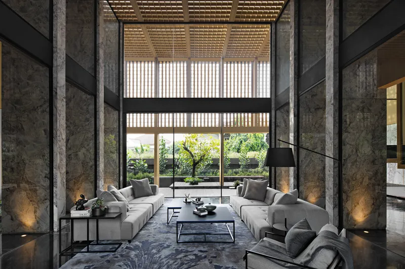 Double-height living space with timber slatted ceiling casting dappled light onto grey stone columns and polished floor