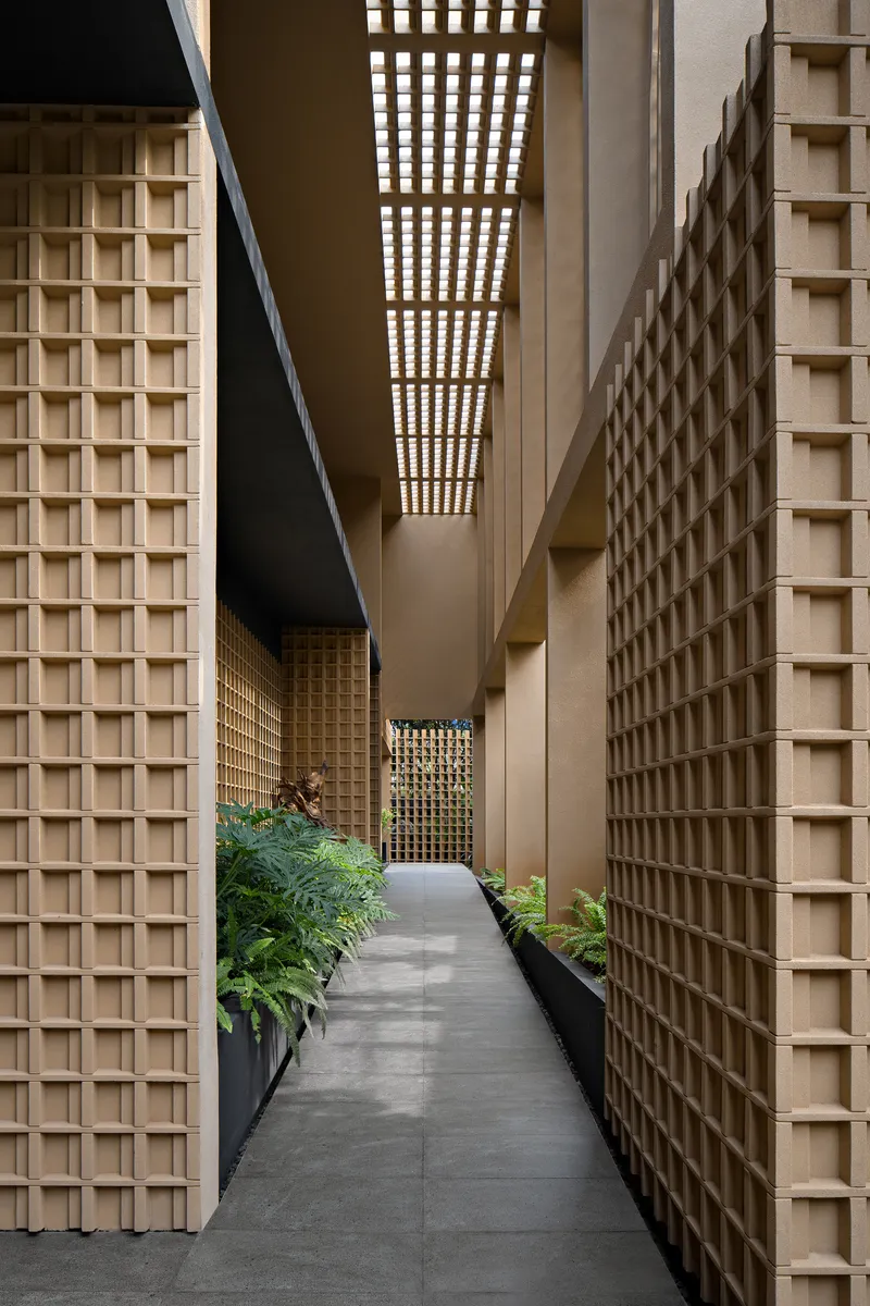 Narrow entrance passageway flanked by timber grid walls and overhead lattice filtering daylight above planters