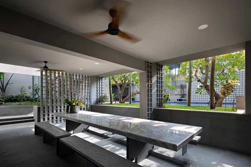 Open-air dining pavilion with stone table and breeze block screens overlooking the garden courtyard