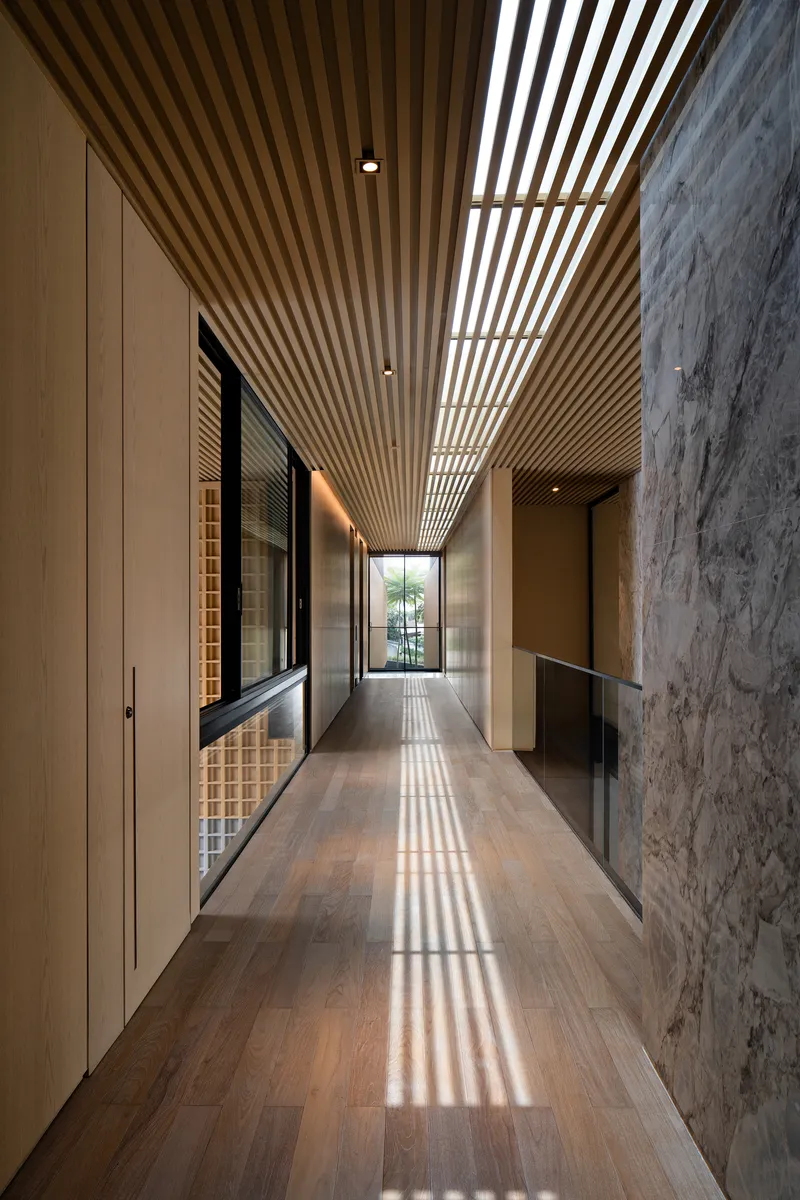 Upper corridor with slatted timber ceiling casting striped shadows onto oak flooring and concrete wall
