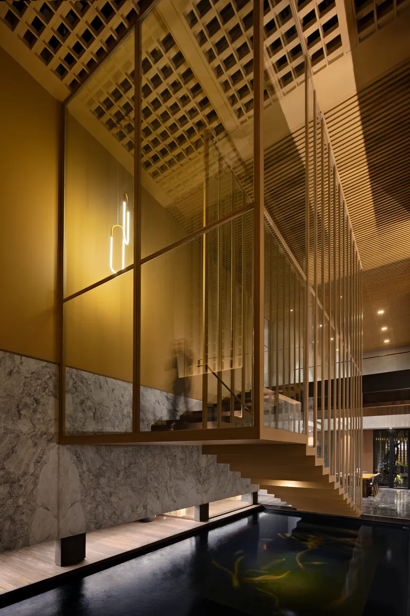 Floating timber staircase with vertical metal rods behind glass, above a dark reflecting pool