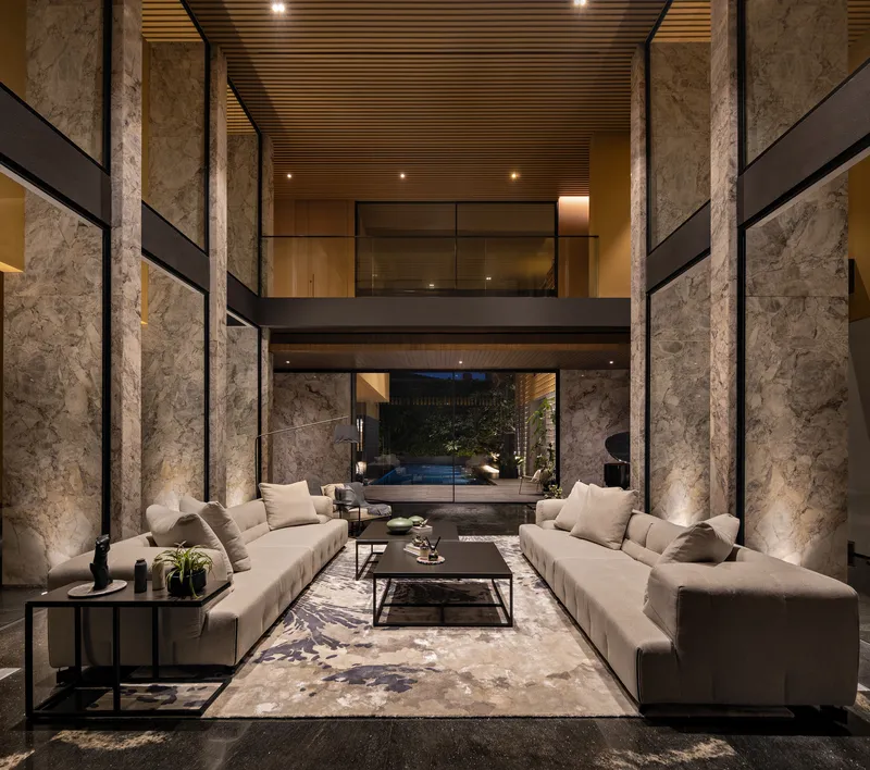 Double-height living space with rough stone columns and slatted timber ceiling under evening light
