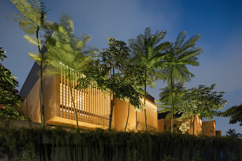 Elevated view of the lattice brick volumes rising above hedge and palm trees at dusk