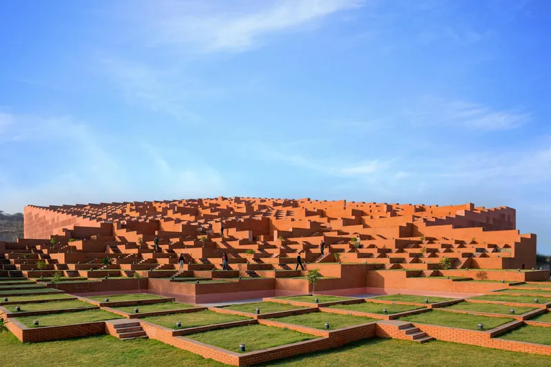 Stepped facade of orange brick volumes cascading down to a grid of lawn courtyards under clear sky
