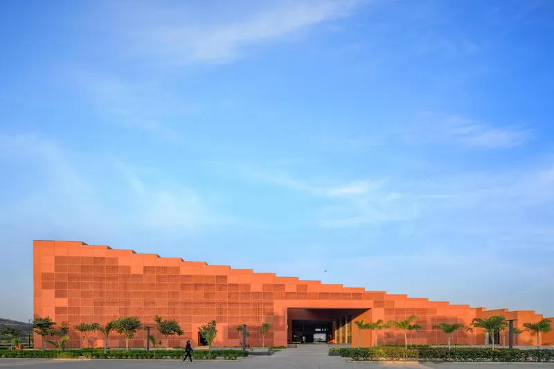 Long facade of pixelated orange brick panels with a central entrance flanked by palm trees