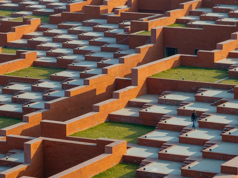 Overhead view of stepped brick terraces with grass courtyards and a solitary figure walking below