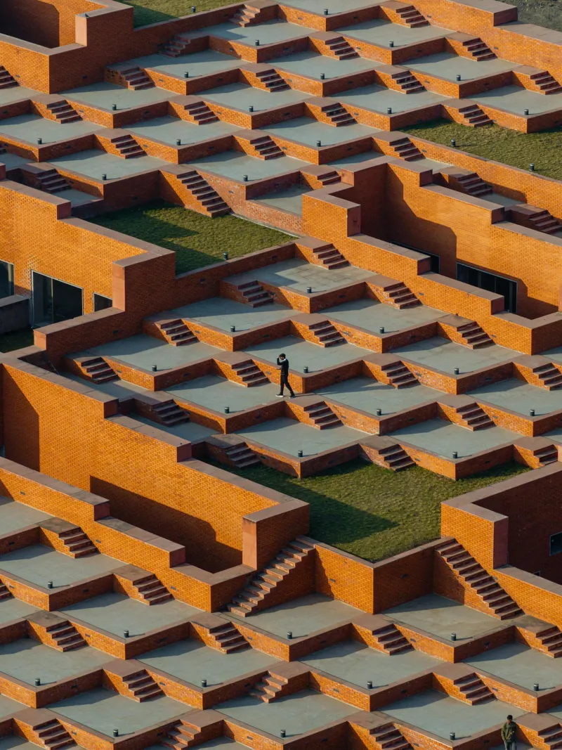 Stepped terraces with orange brick walls and gray concrete platforms connected by stairways with a lone figure