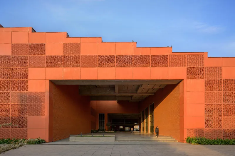 Recessed entrance portal in orange brick facade with stepped massing and perforated screen details above