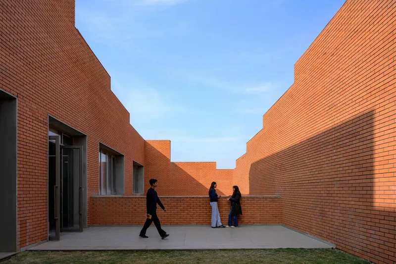 Courtyard enclosed by stepped brick walls with three figures walking in late afternoon light