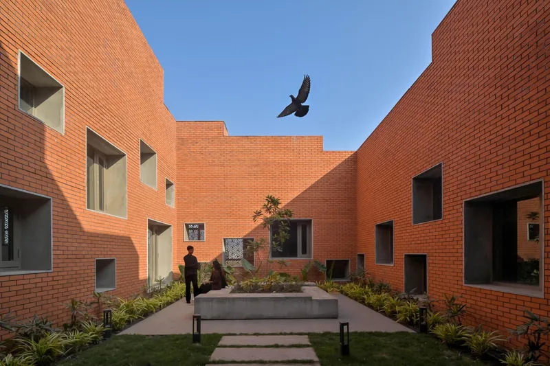 Planted courtyard framed by brick volumes with a bird soaring overhead in clear sky