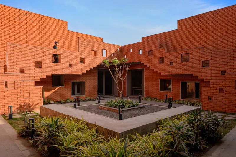 Raised concrete planter bed surrounded by brick walls with scattered window openings at dusk