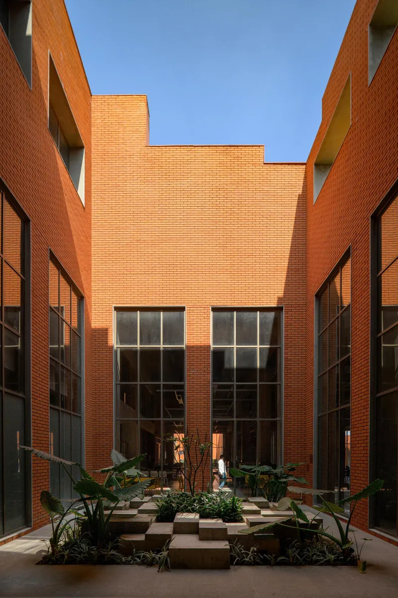 Narrow courtyard passage with tall brick walls and large gridded windows under bright midday sun