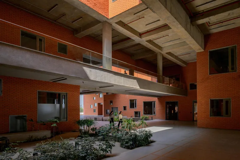 Interior atrium with exposed concrete ceiling, bridge walkway, and planted beds where people gather below