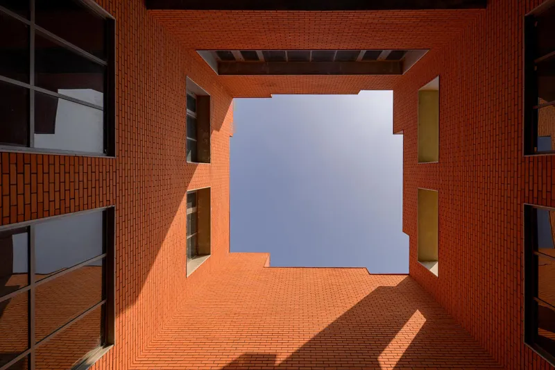 Upward view through a rectangular courtyard framed by orange brick walls and punched window openings