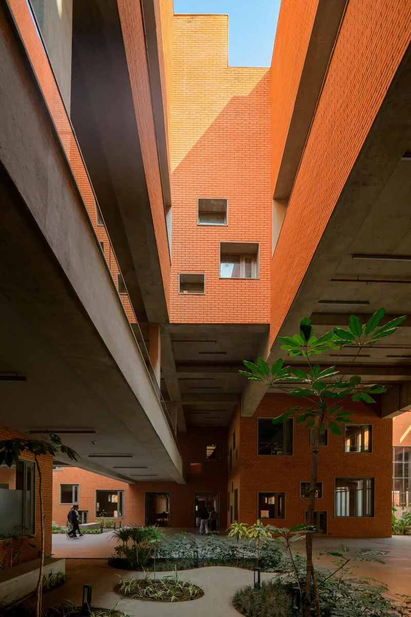 Multi-story courtyard with cantilevered concrete volumes, brick walls and small trees in planters below