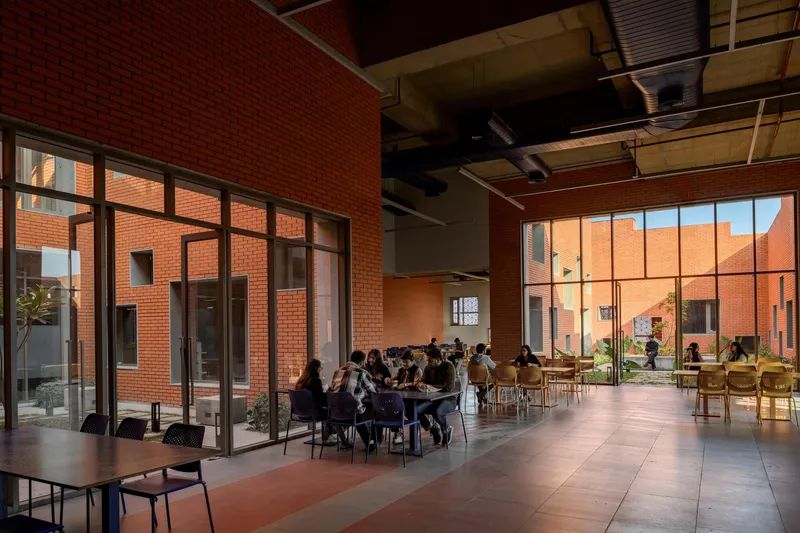 Interior communal space with students seated at tables beneath exposed mechanical systems and timber ceiling panels