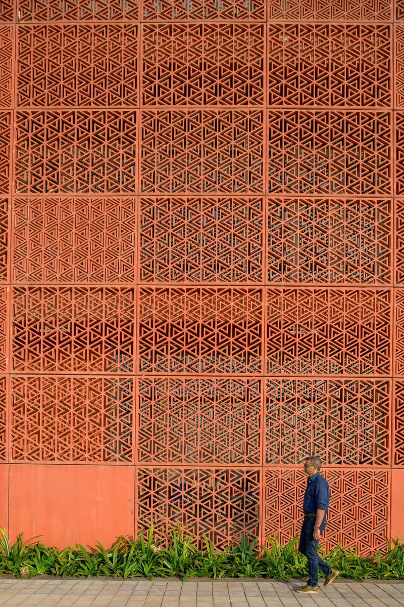 Perforated terracotta brick screen wall with geometric patterning beside a pedestrian walking path