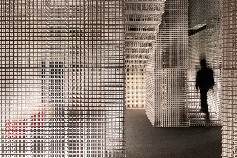 Interior corridor with white perforated mesh walls and ceiling as a figure walks past in shadow