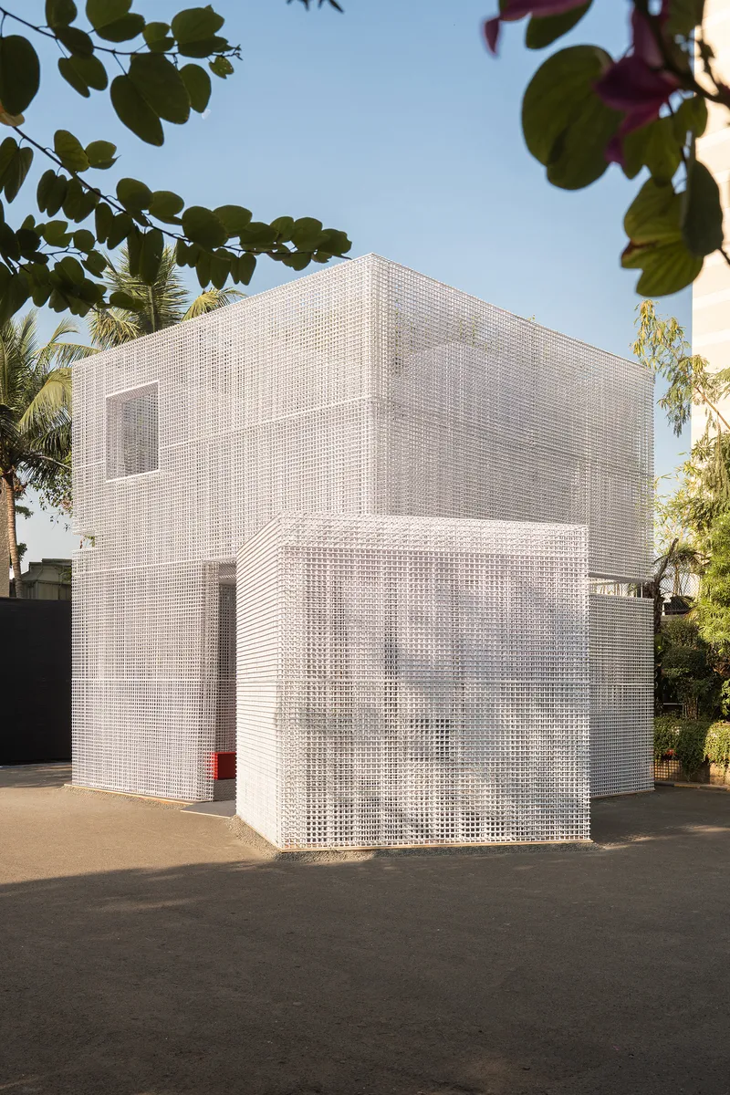 Two-story white gridded mesh facade beneath overhanging palms and leafy trees in afternoon light