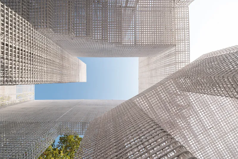 Upward view through the open courtyard framed by perforated screens revealing sky and a small tree