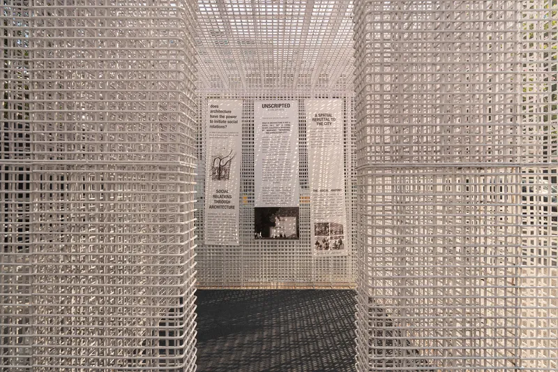 White grid screen enclosure with exhibition panels mounted on the rear wall beneath a perforated ceiling