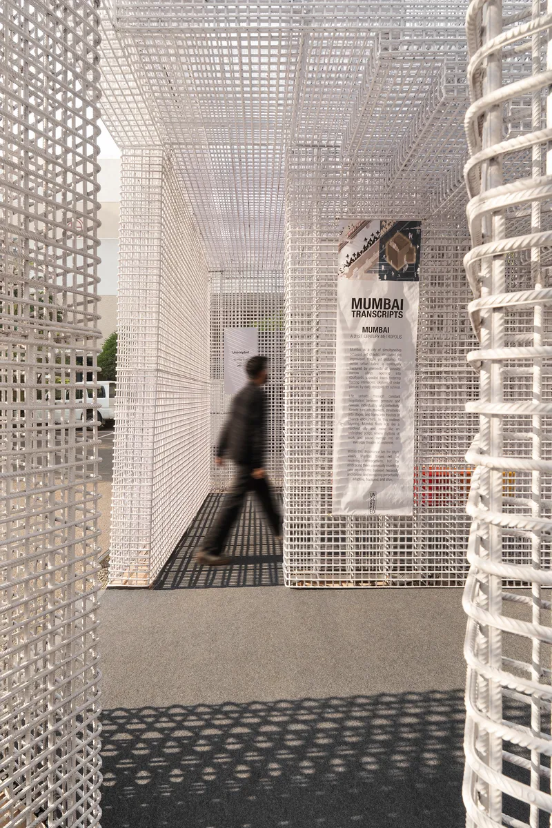 Passageway through white lattice walls with a blurred visitor walking past informational displays and cylindrical column
