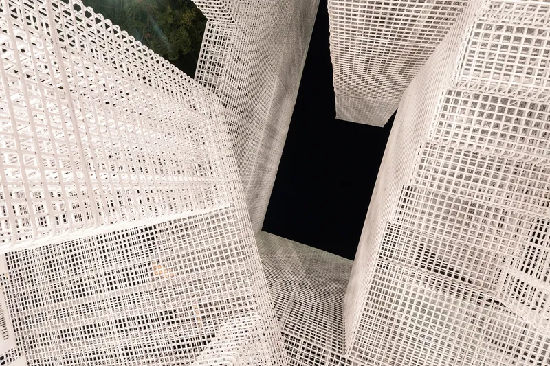 Looking up through white mesh-wrapped volumes intersecting around a dark central void