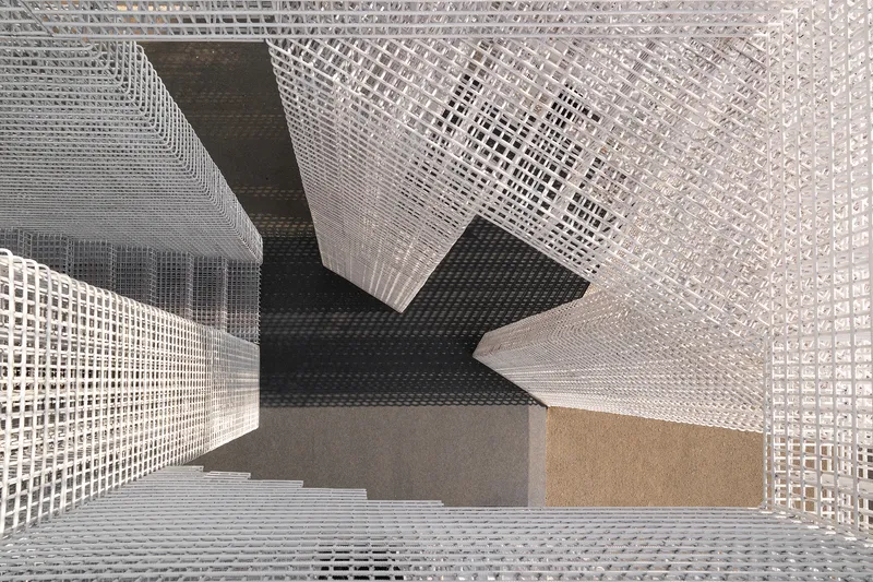 View down into a stairwell surrounded by white grid screens with varied density patterns