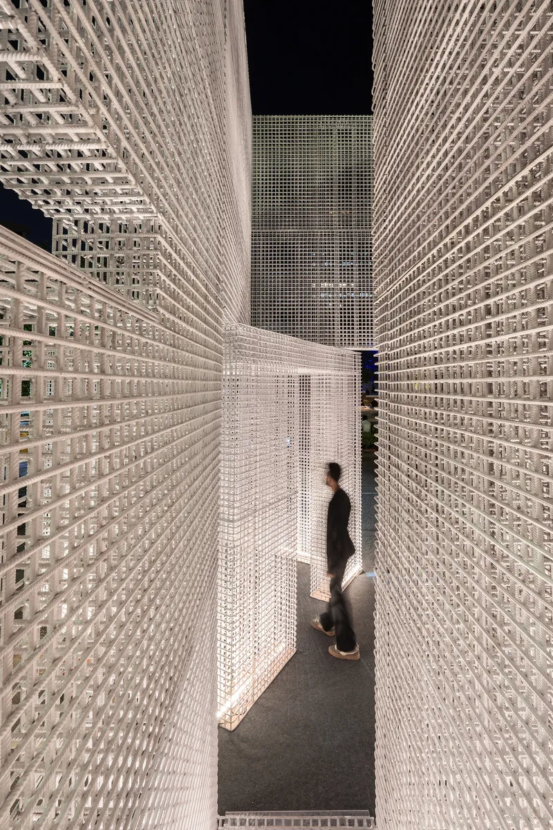 Two visitors walking through a passage framed by floor-to-ceiling white perforated walls