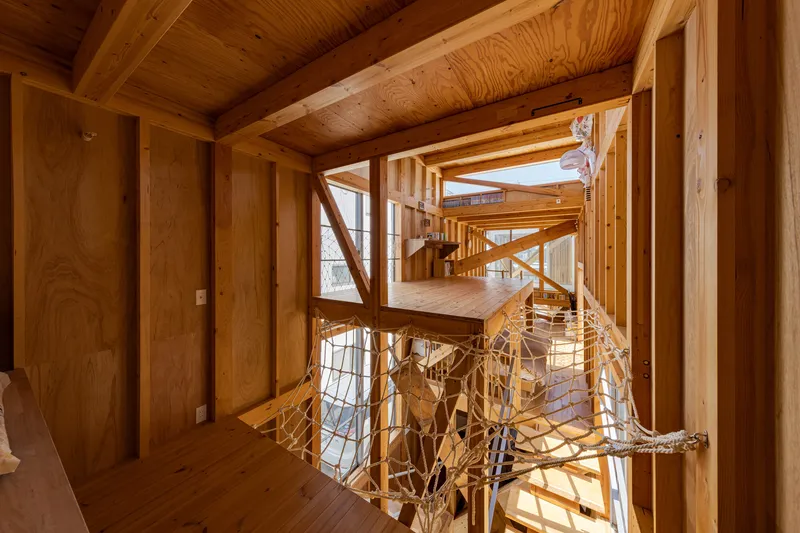 Interior view through timber-framed levels with rope net balustrade and exposed plywood ceiling